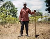 A man standing in a field leaning on a farming tool