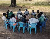 A group of people sitting in a circle outside on blue chairs
